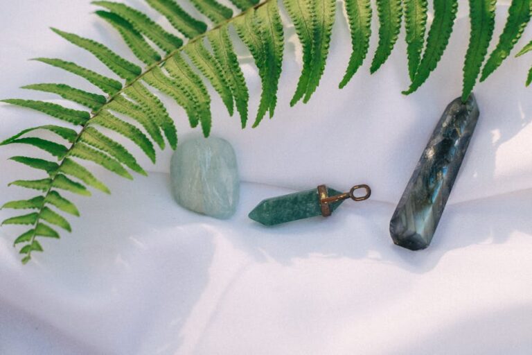 A serene display of healing crystals on white fabric, accented by a fern leaf.